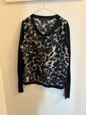 Leopardmönstrad tröja Second Female - Säljer en svart och vit leopardmönstrad tröja från Second Female. Tröjan har långärmade svarta ärmar och ett mjukt, stickat material. Perfekt för dig som vill ha en cool och unik look med lite edge.