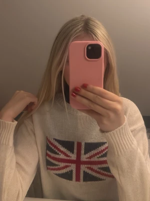 Vit stickad tröja med Union Jack - Säljer en vit stickad tröja med Union Jack-flagga på bröstet. Tröjan har rund halsringning och långa ärmar med ribbade muddar. Perfekt för dig som gillar brittisk stil och vill ha en mysig och snygg tröja till hösten eller vintern.