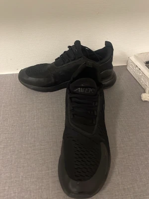 Svarta Nike Air Max 270 sneakers - Säljer ett par helsvarta Nike Air Max 270 sneakers med snygg mesh-överdel och klassisk Air Max-sula. Skorna har snörning och en chunky, rundad form som ger en sportig vibe. Perfekta för dig som gillar stilrena och bekväma sneakers.