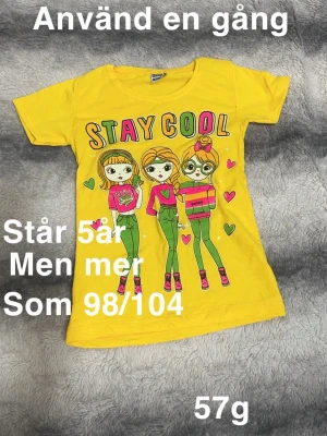 Gul t-shirt med tryck Stay Cool - Gul t-shirt med färgglatt tryck av tre tecknade tjejer och texten 'STAY COOL' på framsidan. T-shirten har korta ärmar och rund hals. 🌸 Använd en gång. Står 5 år men mer som 98/104