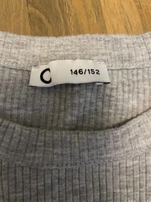 Ljusgrå ribbad långärmad topp - En enkel och stilren ljusgrå ribbad topp med lång ärm och rund hals. Perfekt basplagg i garderoben, lätt att matcha med olika outfits. Tillverkad i mjukt och stretchigt material för skön passform.