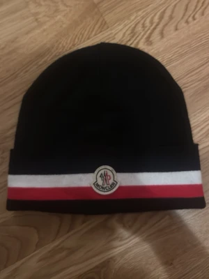 Svart Moncler mössa med ränder - Fraktar direkt, skriv om du är intresserad 👍   Inga skador ✅ Fraktar snabbt ✅ Perfekt Kvalitet ✅