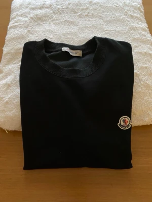 Svart Moncler tröja med logga - Tjo folket! Jag säljer nu den här sköna Moncler tröja. Tröjan är storlek S men passar även M. Den har två klassiska loggor, en på axeln och den andra på vänster sida bröst. På axeln har den även en vit logga. Materialet är bomull, perfekt för våren som nu är bakom hörnet. Priset kan diskuteras, skriv för minsta fråga!