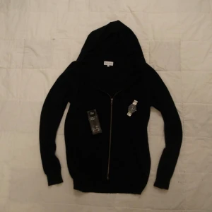 Svart hoodie i kashmir från Davida - Svart hoodie från Davida i mjuk kashmir. Tröjan har dragkedja framtill, huva och långa ärmar. Perfekt för dig som vill ha en stilren och bekväm look med lyxig känsla. Passar lika bra till jeans som till mjukisbyxor.