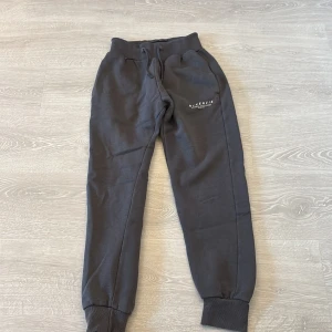 Mörkgrå mjukisbyxor från McKenzie - Mörkgrå mjukisbyxor från McKenzie med resår och snörning i midjan. Byxorna har ribbade muddar vid bensluten och två sidofickor. Perfekta för chill eller träning, med diskret logga på ena benet. Tillverkade i mjukt material för extra komfort.