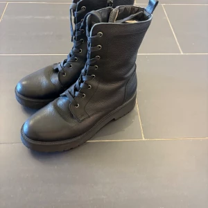 Svarta vinterfodrade kängor i skinn med snörning - Snygga svarta varmfodrade kängor i äkta skinn med grov sula och snörning hela vägen upp. Klassisk rund tå och robust design som passar perfekt till höst och vinter. Stilrena och lätta att matcha med olika outfits.