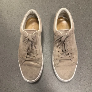 Beige mockasneakers från Vagabond - Snygga beige sneakers från Vagabond i mjuk mocka med klassisk rund tå och vita sulor. Skorna har snörning och stilren design som passar till det mesta. Perfekta för dig som gillar en clean och enkel look. Endast använda en sommar, bra skick! Nypris 1400kr