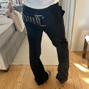 Svarta Juicy Couture mjukisbyxor - Svarta mjukisbyxor från Juicy Couture i mjuk sammet med glittrande strasstext på baksidan. Byxorna har snörning i midjan och raka ben. Perfekta för en chill och trendig look.