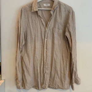 Beige linneskjorta från Uniqlo L - Luftig och stilren beige skjorta från Uniqlo i 100% linne. Skjortan har klassisk krage, bröstficka och knäppning framtill. Perfekt för varma dagar och enkel att styla till jeans eller shorts. 