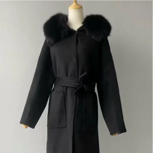 Svart kappa med päls från FUR Stockholm - Snygg svart kappa från FUR Stockholm med fluffig päls runt kragen och huva. Kappan har bälte i midjan, stora fickor och knappar framtill. Långärmad och med en stilren, rak passform som ger en cool vibe. Perfekt för dig som vill ha en statement piece i garderoben. OBS! Den är använde och en knapp har gått av! Kappan består av 90% ULL och 10% kashmir, pälskragen består av 100% rävpäls. 