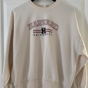 Beige Harvard sweatshirt från H&M - Oversized beige sweatshirt från H&M med tryck 'Harvard University' i rött och svart framtill. Mjuk insida, ribbade muddar vid ärmslut och nederkant. Perfekt för en chill och avslappnad look.