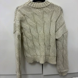 Beige stickad tröja från NA-KD - Säljer en chunky beige stickad tröja från NA-KD i storlek XXS/XS, passar även dig som bär storlek S. Tröjan har ett grovt kabelstickat mönster, ribbade muddar och hög hals. Perfekt för lager-på-lager och en mysig vibe under kyliga dagar. Aldrig kommit till användning. 