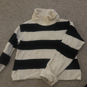 Randig polotröja från Lindex - Säljer en stickad polotröja från Lindex i storlek S. Tröjan har breda svarta och vita ränder, hög polokrage och långa ärmar. Sparsamt använd.