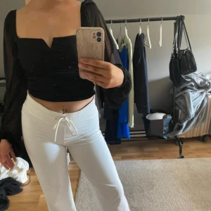 Svart croppad topp med meshärmar - Säljer en svart croppad topp med långa meshärmar som kan bäras både offshoulder och på axlarna. Toppen har en snygg v-ringning med liten kant framtill och är figurnära i modellen. Perfekt för dig som gillar trendiga detaljer och en stilren outfit.