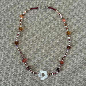 Pärlhalsband - Unikt halsband med små pärlor i rött, vitt och brunt samt större glaspärlor i orange och brunt. I mitten sitter en blomformad pärla, perfekt till hösten med höstiga färger, halsbandet är 40cm långt. 