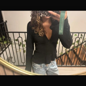 Svart omlottopp från Gina Tricot XS - Svart omlottopp från Gina Tricot i storlek XS. Toppen har lång ärm, djup v-ringning och knytband i ryggen. Materialet är mjukt och lätt ribbat, vilket ger en snygg struktur🩷