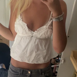 Vit croppad linnetopp från Zara XS - Supersöt vit croppad linnetopp från Zara med tunna axelband och snörning framtill. Toppen har volangdetaljer vid bysten och en v-ringad urringning. Perfekt för varma dagar och har en luftig passform. Materialet är lätt och känns skönt mot huden.