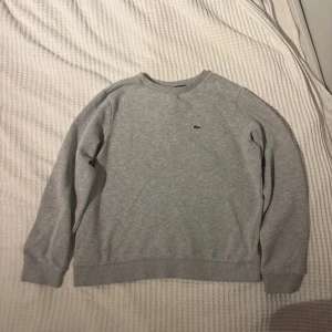 Grå sweatshirt från Lacoste -  Storlek 164cm  14 år Snygg grå sweatshirt från Lacoste med klassisk rund hals och det lilla gröna krokodilmärket på bröstet. Skick 8/10 väldigt bra skick enbart använd därför skick 8/10 