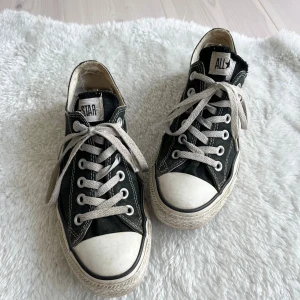 Svarta Converse All Star sneakers - Klassiska svarta Converse All Star sneakers med vit tå och sula. Skorna har lågt skaft, vita snören och tydliga kontrastsömmar. Ovandelen är i canvas och sulan i gummi, med All Star-logga bak på hälen. Perfekta för en avslappnad och cool stil.
