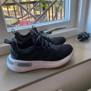 Adidas Cloudfoam svarta sneakers - Svarta Adidas Cloudfoam sneakers med mesh-ovandel, vita och bruna sulor samt klassiska tre ränder på sidan. Skorna har snörning och en chunky sula med dämpning för extra komfort. Perfekta för dig som gillar sportig och stilren look.