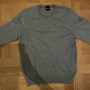 Grå tröja från BOSS i merinoull - Snygg grå tröja från BOSS i mjuk ullblandning. Klassisk rund halsringning och ribbade muddar vid ärmslut och nederkant. Egentligen aldrig använd så mycket bra pris med tanke på skicket samt nypriset tröjan har.🔥