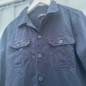Overshirt mörkblå - Stilren mörkblå overshirt från Hampton Republic med klassisk krage, två bröstfickor med lock och knappar framtill | Skulle säga att den passar för ca 175-182 | Om du har några fler funderingar är det bara att fråga 👍