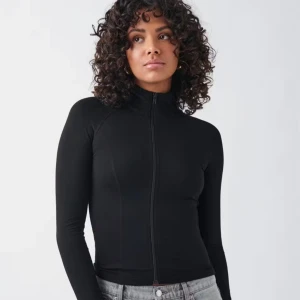 Svart tight ziptröja med lång ärm - Svart långärmad ziptröja med hög krage och hel dragkedja framtill. Sitter tight och har en clean, minimalistisk look som passar perfekt till jeans eller leggings. Enkel och stilren design utan synliga loggor eller detaljer.