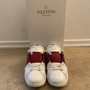 Valentino Garavani Open sneakers vit/röd - Säljer ett par Valentino Garavani Open sneakers i vitt skinn med bred röd läderdetalj över mitten. Klassisk rund tå, snörning och ikoniska nitar baktill på sulan. Enda defekten är undersidan på skon. Perfekta till hösten. Galet bra pris om du frågar mig!😮‍💨 det enda som är synligt på användning är hälen som är lite ner sliten men inga hål eller sånna defekter. Tveka inte att höra av dig vid minsta fundering👊 priset är diskuterbart! Passar storlek 41. Köpta på NK i Gbg