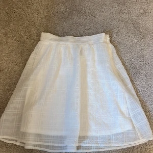 Vit långkjol från H&M Divided - Säljer en vit långkjol från H&M Divided i storlek 32. Kjolen har ett diskret rutigt mönster i tyget, är lätt och luftig med dragkedja i sidan. Perfekt för en fräsch och stilren look under varmare dagar.