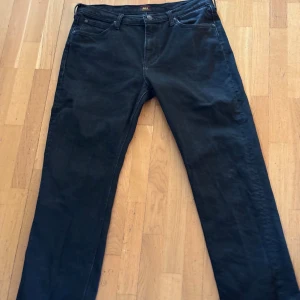 Svarta Lee jeans straight fit - Svarta jeans från Lee med klassisk femficksdesign och raka ben. Jeansen har en enkel look med Lee-logga på bakfickan och är tillverkade i ett slitstarkt jeanstyg. Perfekt för dig som gillar stilrena och tidlösa byxor.