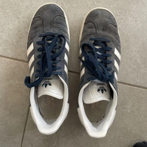 Adidas Gazelle mörkblå sneakers - Säljer ett par klassiska Adidas Gazelle sneakers i mörkblå mocka med vita detaljer, lite slitnare färgen men annars hela.