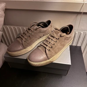 Lanvin sneakers i mocka och skinn - Snygga sneakers från Lanvin i grå mocka med matchande beige skinn på tån och snörning. Klassisk rund tå och platt sula i offwhite. Perfekta för dig som gillar stilrena och exklusiva skor med en lyxig känsla. Små slitage, pris går att diskutera 