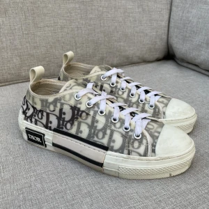Dior skor - Säljer ett par Dior B23 sneakers med genomskinligt material och ikoniskt Dior-monogram i svart och grått. Skorna har vita snören, vit sula och svarta detaljer på sidan. Perfekt för dig som vill sticka ut med en lyxig och modern look.