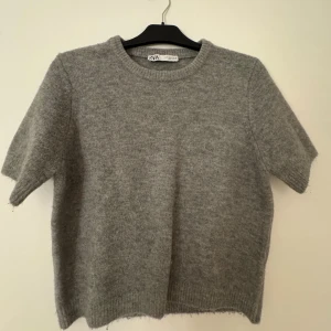 Grå stickad tröja från Zara - Är storlek L men sitter perfekt på mig som är stolek S-XS. Mysig grå stickad tröja från Zara med korta ärmar och rund hals. Tröjan har en enkel och clean look med ribbade detaljer vid hals och nederkant. Perfekt för dig som gillar basic och vill ha något som funkar till många olika stilar.