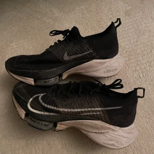 Nike Air Zoom Tempo Next % Flyknit Joggingskor (Storlek 41)  - Svart/vit Nike air zoom tempo next % flyknit i fint skick! Har Nikes Swoosh-logotyp, Flyknit-textur, rund tå, snörning i fram, dragögla baktill, innersula med logotyp, innersula med logotyp, grov gummisula. Nypris 3700kr. 