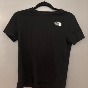 Svart t-shirt från The North Face - Svart t-shirt från The North Face med klassisk logga tryckt på bröstet. Enkel och stilren design med rund hals och korta ärmar. Perfekt för dig som gillar streetwear och vill ha en basic tee med snygg branding.