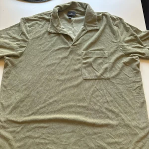 Olivgrön frotté tröja från H&M - Olivgrön frotté från H&M i storlek XXL. Tröjan har klassisk krage, korta ärmar och en bröstficka. Materialet är mjukt och frottéliknande, vilket ger en chill och avslappnad vibe. Perfekt för vår och sommar när du vill vara bekväm men ändå se fräsch ut.