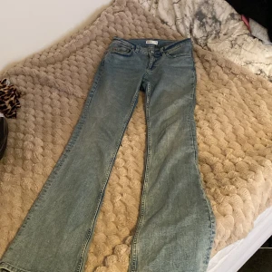 Ljusblå bootcut jeans med låg midja - Säljer ett par ljusblå jeans från Gina Tricot med bootcut-modell och låg midja. Jeansen har klassiska fem fickor, dragkedja och knapp framtill samt breda ben nertill. Perfekta för dig som gillar retrovibbar och snygg passform.