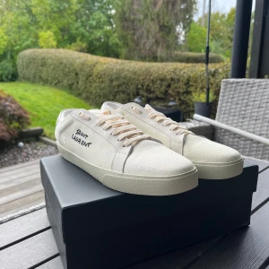Saint Laurent vita sneakers i canvas - Snygga vita sneakers från Saint Laurent med handskriven logga på sidan. Skorna har en klassisk låg profil, beige snörning och ovandel i canvas med detaljer i skinn. Perfekta för dig som gillar stilrena och exklusiva sneakers med en clean look. Priset är ej hugget i sten och om du har en fråga? Fråga på :)
