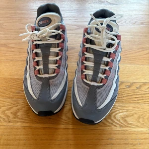 Nike Air Max 95 grå/vit sneakers - Nike Air Max 95 sneakers i grått och vitt med inslag av rostrosa detaljer. Skorna har en chunky sula med synlig Air Max-dämpning, mesh och syntetmaterial på ovandelen samt snörning framtill. Perfekta för dig som gillar en sportig och retro vibe.