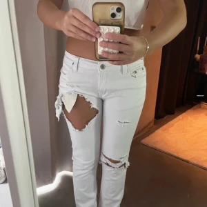 Vita jeans - Säljer ett par vita jeans med stora slitningar och hål på låret och knäet. Modellen har klassisk femficksdesign, raka ben och normal midja. Jeansen är gjorda i bomull och har en lågmidja längd: 78 midja: 38