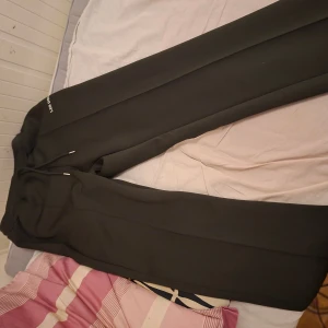 Svarta mjukisbyxor från Les Deux - Svarta mjukisbyxor från Les Deux med stilren design och diskret logga på benet. Byxorna har snörning i midjan och raka ben, tillverkade i mjukt material som känns skönt mot huden. Perfekta för chill dagar eller när du vill ha en clean look.