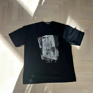 Svart t-shirt från Yohji Yamamoto - Svart t-shirt från Yohji Yamamoto Pour Homme med unik grafisk print framtill i vitt och lila toner. Klassisk passform med rund hals och korta ärmar. Tillverkad i mjuk bomull som känns skön mot huden. Perfekt för dig som gillar statement-plagg med konstnärlig vibe. Väldigt oversize! Köpt på vinted! 