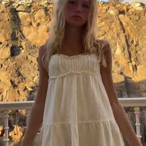 Vit somrig klänning från Zara - Superfin vit klänning från Zara med smockad överdel och volangdetaljer. Klänningen är ärmlös och har en luftig, flowy passform som är perfekt för varma dagar. Tillverkad i mjukt bomullstyg och har en romantisk känsla.