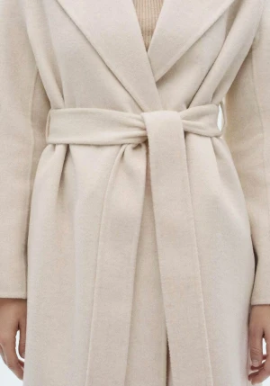 Beige omlottkappa med bälte från Mango - Snygg beige kappa från Mango med brett bälte i midjan. Jackan har klassisk krage, långa ärmar och en stilren, rak siluett. Materialet är mjukt och känns lyxigt, perfekt för dig som gillar minimalistisk och clean stil.