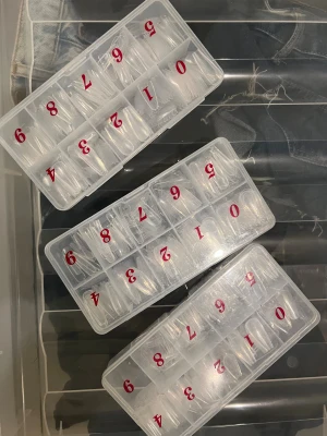 Falska nageltippar i olika storlekar - Säljer flera askar med transparenta nageltippar i olika storlekar, perfekt för att skapa egna gel- eller akrylnaglar. Tipparna är gjorda av plast och kommer i organiserade fack med röda siffror för enkel användning. Passar både till salong och hemmafix. Cirka 1300 st 