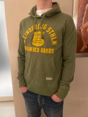 Grön vintage hoodie från J.Lindeberg - Snygg grön hoodie från J.Lindeberg med gul text och emblem på bröstet. Passar som en M storlek. Tröjan har huva med snörning, stor magficka och långa ärmar. Vintage plagg som är väldigt svår att få tag på. Passar också mindre L.