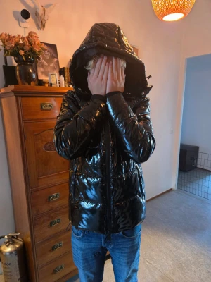 Svart pufferjacka från Ellesse XS - Säljer en svart, glansig pufferjacka från Ellesse i storlek XS. Jackan har huva, dragkedja framtill och quiltad design som ger en cool vibe. Perfekt för kalla dagar och riktigt snygg till jeans eller cargo. Materialet är syntet och jackan är riktigt lätt att bära.