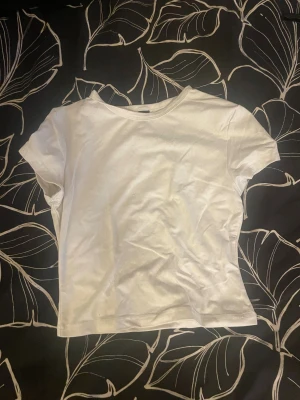 Vit kortärmad topp från SHEIN XS - Säljer en enkel och fräsch vit topp från SHEIN i storlek XS. Modellen är kortärmad med rund hals och har en rak, normal passform. Materialet är mjuk bomull som känns skönt mot huden. Perfekt att styla med jeans eller kjol för en clean look.