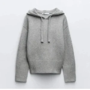 Grå stickad hoodie med huva - Mysig grå stickad hoodie med huva och snörning framtill. Tröjan har långa ärmar och bred ribbad kant vid midjan och ärmsluten. Perfekt för dig som gillar en chill och enkel stil.